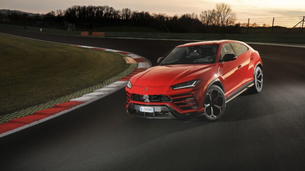 A red Lamborghini Urus driving on a race track during sunset
