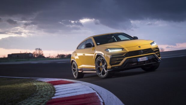 Yellow Lamborghini Urus driving on a race track under a cloudy sky
