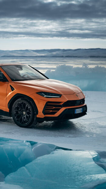 Orange Lamborghini Urus parked on icy terrain with mountains in the background