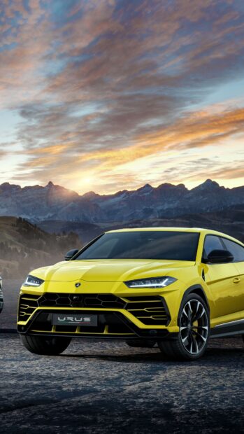 Yellow Lamborghini Urus driving on mountain road at sunset with scenic mountain background