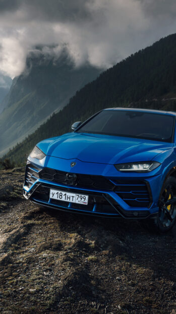 Blue Lamborghini Urus parked on a rugged mountain terrain under cloudy skies
