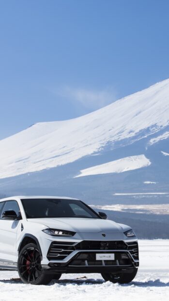 White Lamborghini Urus parked on snowy terrain with mountains in the background