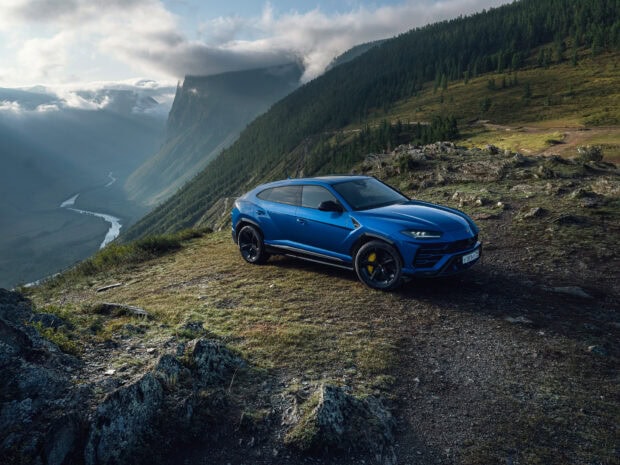 Blue Lamborghini Urus parked on a mountain side with a scenic valley view in the background