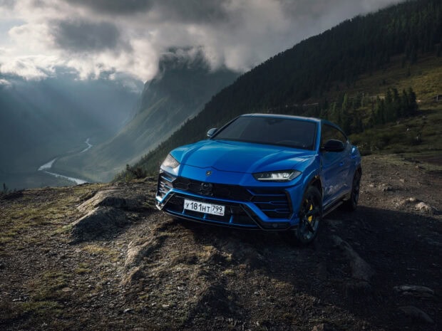 Blue Lamborghini Urus parked on a rocky terrain with mountains and dramatic clouds in the background