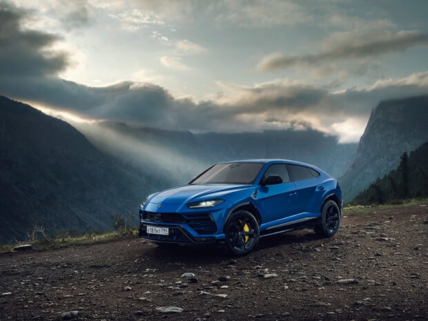 Blue Lamborghini Urus parked on mountain dirt road with dramatic cloudy sky background