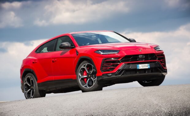 Red Lamborghini Urus parked on a hill with a cloudy sky background
