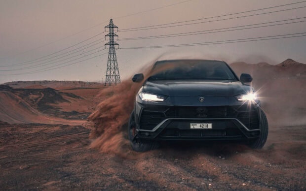 Black Lamborghini Urus driving fast on a dirt road kicking up dust in a desert environment