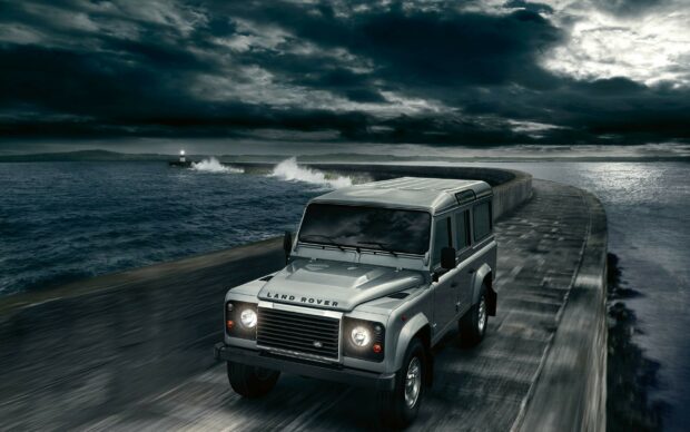 Land Rover driving on a curved ocean pier under stormy skies at night