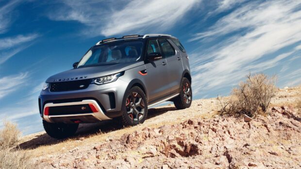 A Land Rover Discovery driving on a rocky hill against a blue sky with scattered clouds
