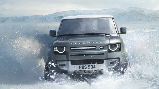 Land Rover Defender driving through snowy terrain with snowy mountains in the background