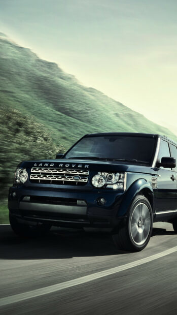 A Land Rover driving fast on a mountain road with green hills in the background