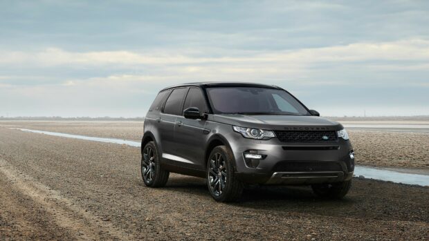 A sleek Land Rover vehicle parked on a rocky beach under a cloudy sky