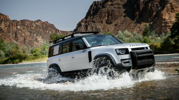 Land Rover driving through river water in mountain landscape
