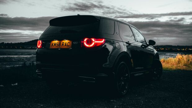 Land Rover parked near a lake during twilight with glowing tail lights and cloudy sky