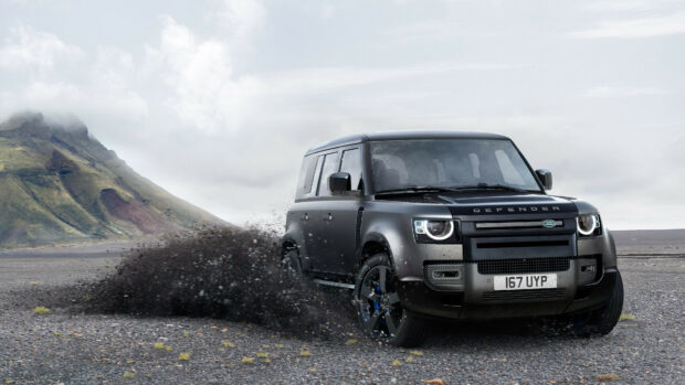A Land Rover Defender driving fast on a rocky terrain with mountains in the background