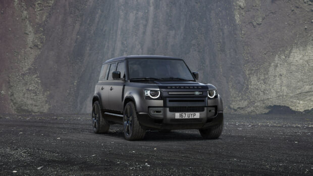 Matte black Land Rover Defender parked on rocky terrain with mountain background