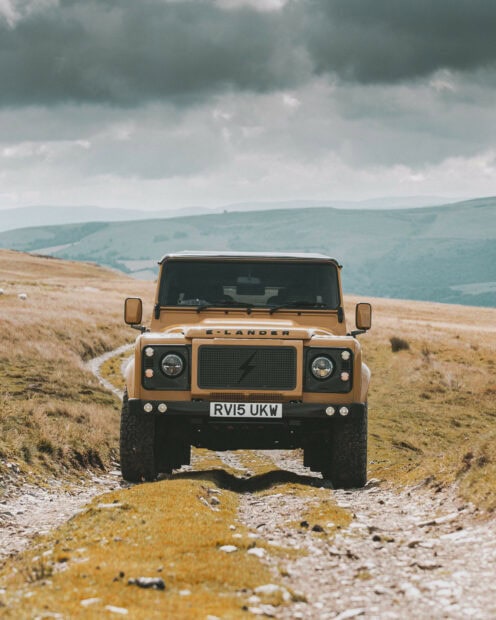 Yellow Land Rover driving on a rocky countryside road with hills in the background