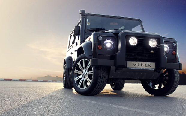 Black Land Rover on an empty road at sunset with headlights on