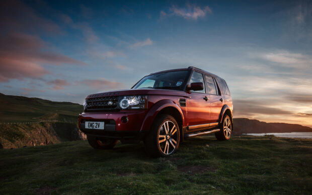 Red Land Rover parked on grassy hill during sunset with scenic background