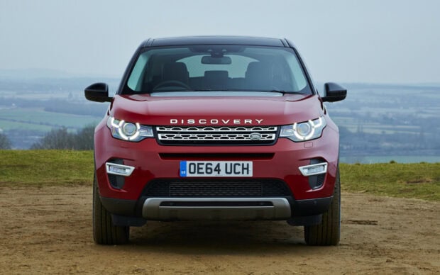Red Land Rover vehicle front view with Discovery badge on a dirt road