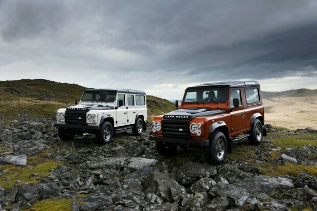 Two Land Rover vehicles parked on rocky terrain under a cloudy sky in a rugged landscape