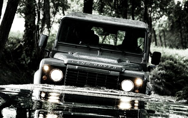 Land Rover crossing a river in a forest with headlights on in high quality