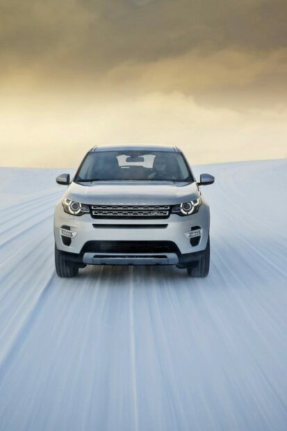 White Land Rover driving on snowy terrain under cloudy sky