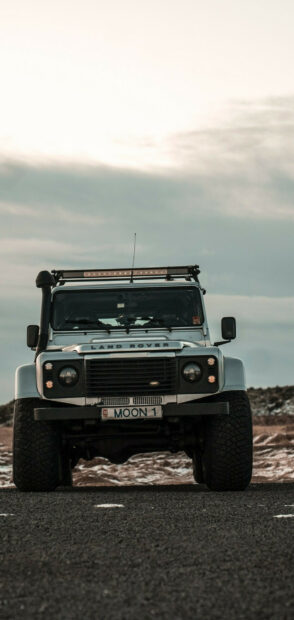 White Land Rover vehicle parked on a road with cloudy sky in the background
