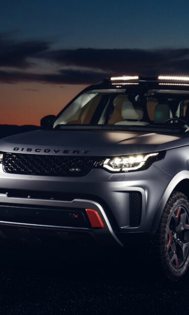 Land Rover Discovery parked at dusk with bright headlights and roof lights