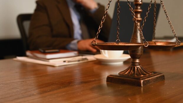 A lawyer scales on a wooden desk with a person working in the background
