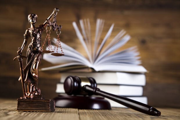 Bronze statue of justice with scales and gavel on wooden table with law books