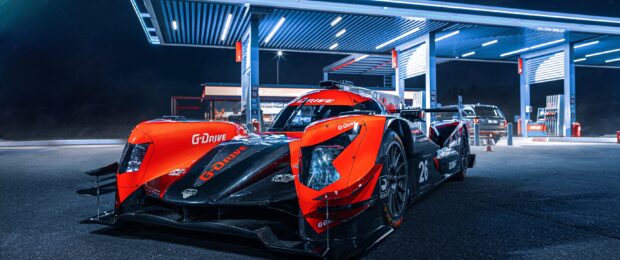 A red and black Le Mans race car parked at a gas station at night with a clear sky