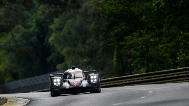 Black race car number 2 speeding on Le Mans track surrounded by trees