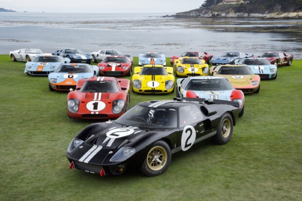 Classic Ford race cars lined up on green grass near the sea at Le Mans