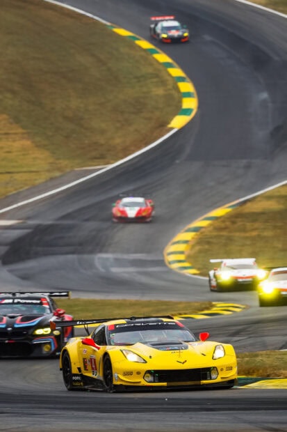 Yellow race car leading the pack on a curvy Le Mans race track in high speed