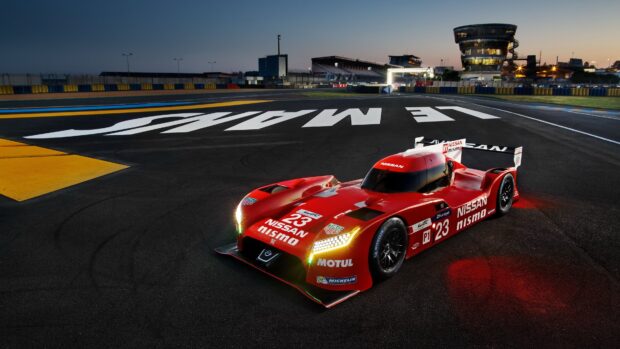 Red Nissan race car at Le Mans racing circuit during dusk with track and grandstand visible