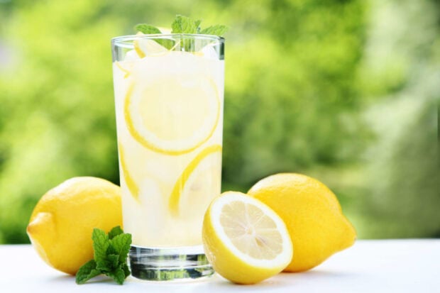 A fresh lemonade drink with lemons and mint leaves on a white surface