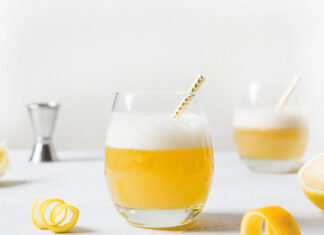 A fresh glass of lemonade with foam and a striped straw on a white surface