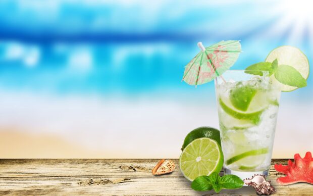 A refreshing lime drink with ice and mint on a wooden table by the beach
