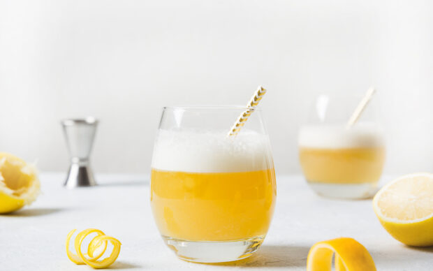 A fresh glass of lemonade with foam and a striped straw on a white surface