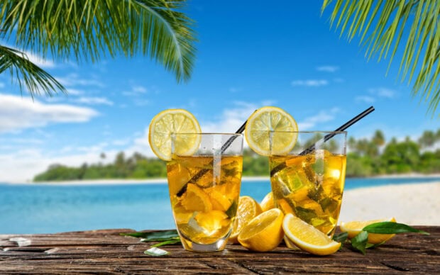 Two refreshing lemonade drinks with lemon slices on a wooden table at the beach