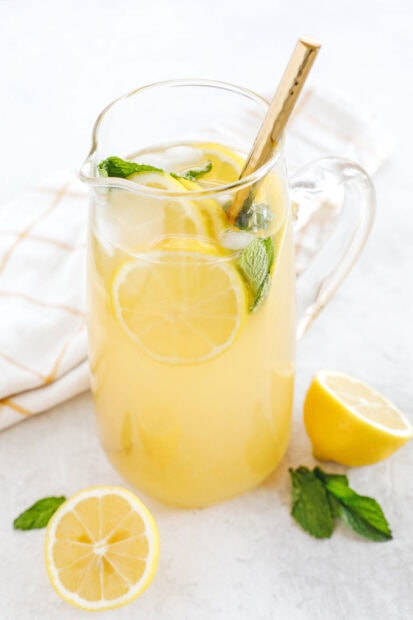 A refreshing lemonade drink with lemon slices and mint leaves in a glass pitcher