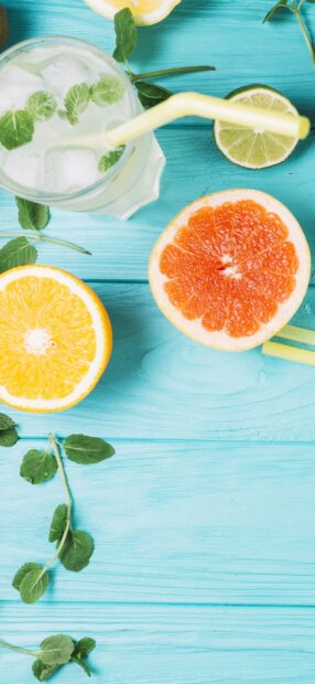 Fresh citrus fruits and ice drink on turquoise wooden table with mint leaves