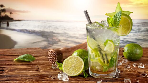 A refreshing lemonade with lime slices and mint leaves on a wooden table near the beach at sunset