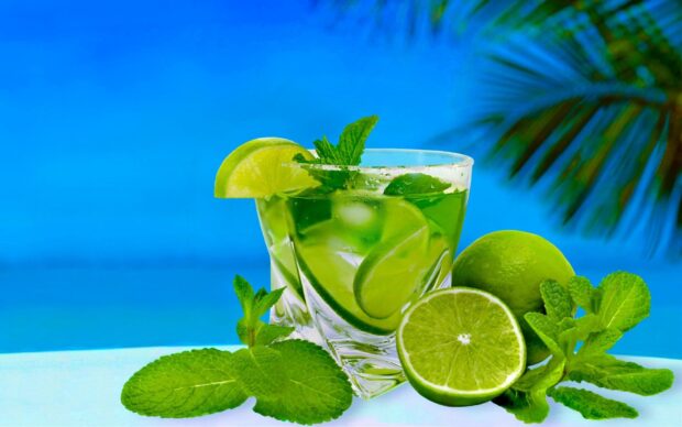 A refreshing lemonade drink with lime slices and fresh mint leaves on a bright blue background
