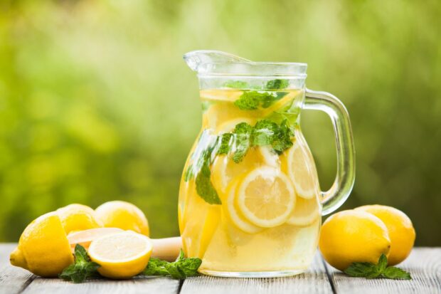 A refreshing pitcher of lemonade with lemon slices and mint leaves on a wooden table