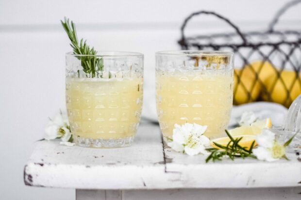 Two glasses of fresh lemonade with rosemary and flowers on rustic white table