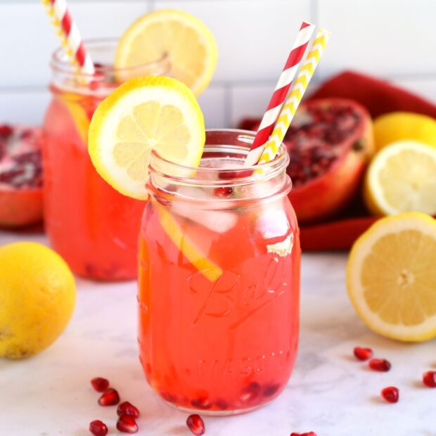 A refreshing lemonade drink with lemon slices and pomegranate seeds in a mason jar with colorful straws