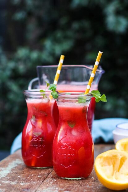Fresh lemonade with mint leaves served in glass jars with yellow straws on wooden table