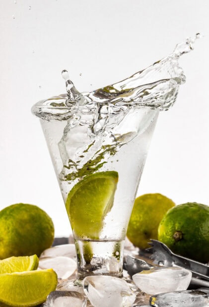 Fresh lime slice splashing into a glass of water with ice cubes and limes around